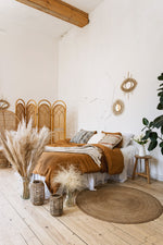 Bohemian style decor bedroom.  Light brown duvet, light brain plants in rustsic vasses.  Wicker furniture.
